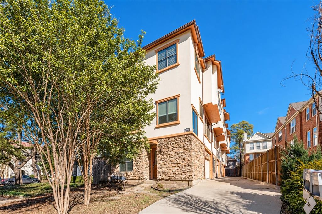 Multi-story stucco exterior with stone accents, multiple windows, and a paved driveway