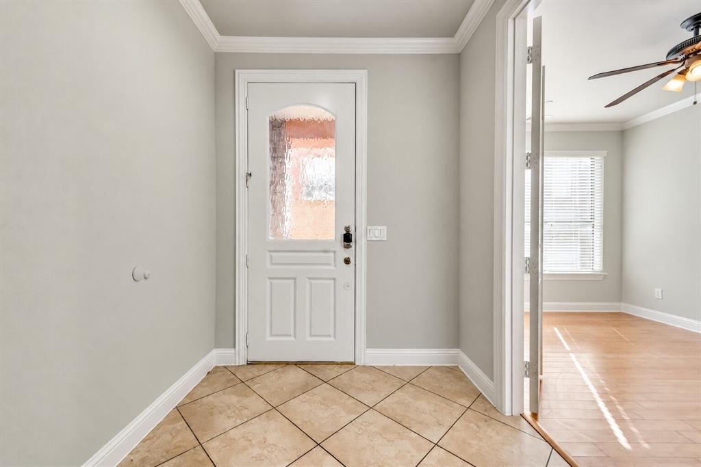 Entryway featuring ceramic tile flooring, a white paneled door with decorative glass, crown molding, and light-colored walls