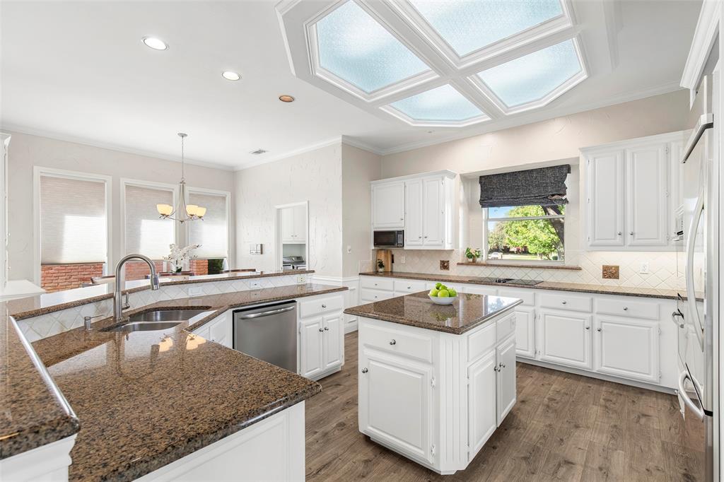 White cabinetry, granite countertops and a center island provide generous storage and preparation space beneath a distinctive ceiling light feature.