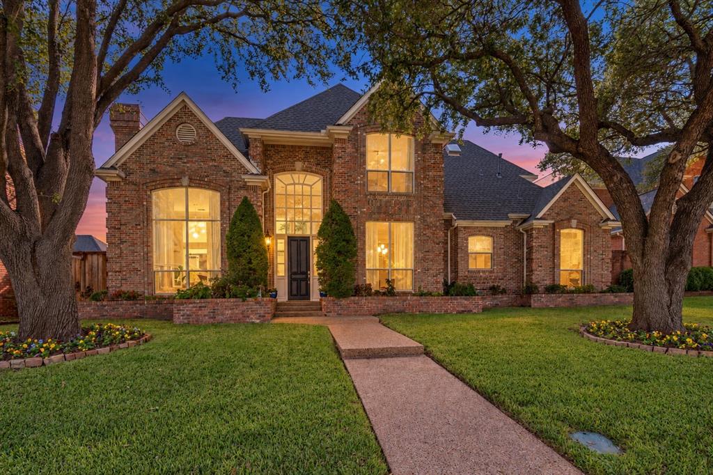 There’s something special about coming home to this. Warm windows glow beneath a twilight sky, while mature trees frame the classic brick exterior and a welcoming walkway leads you to the front door.