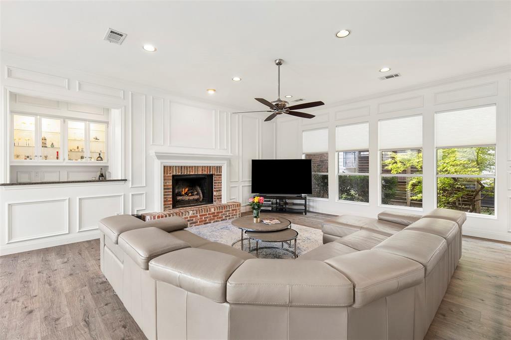 An inviting brick fireplace and soaring ceilings anchors this sunlit family room, complete with an adjacent built-in entertaining bar and custom wall paneling that frames the ideal gathering space.