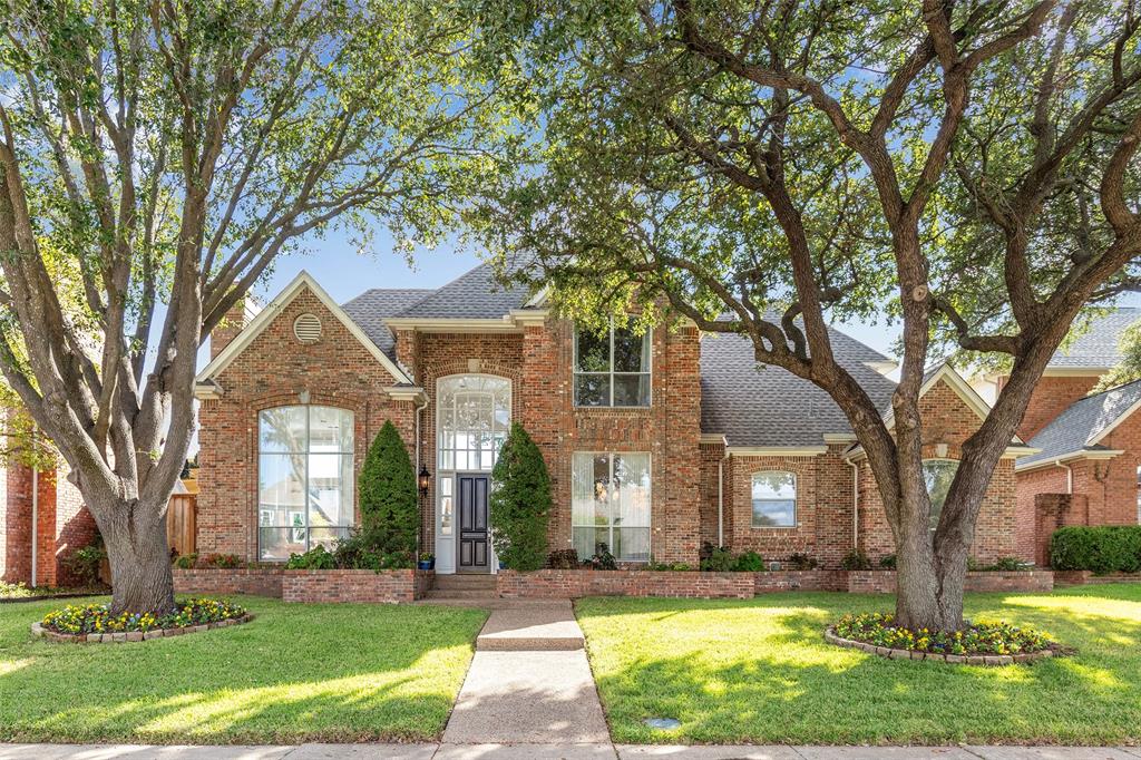 Mature shade trees frame the classic brick exterior, landscaped beds and welcoming front walk at 4324 Highlander Drive
