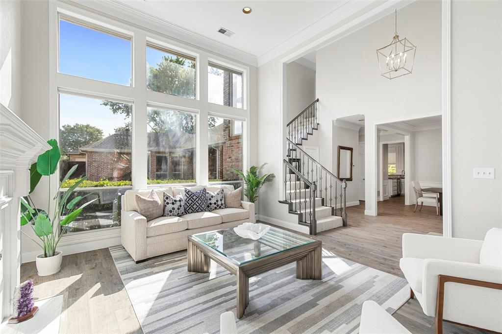 Soaring double-height ceilings and a dramatic wall of windows flood the formal living space with natural light, creating a bright and airy atmosphere anchored by a classic fireplace.