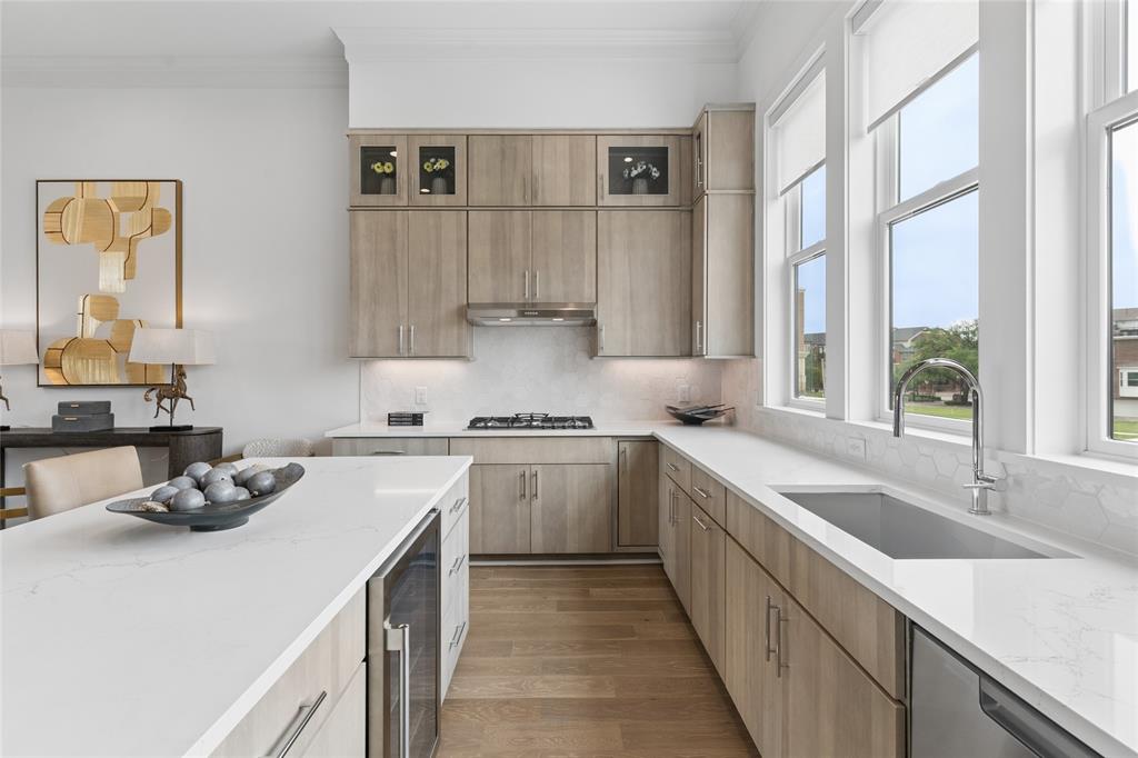 The kitchen is flooded with natural light and offers stacked upper cabinetry, Fisher & Paykel appliances, quartz surfaces and a designer tile backsplash. Image of model home with similar layout.