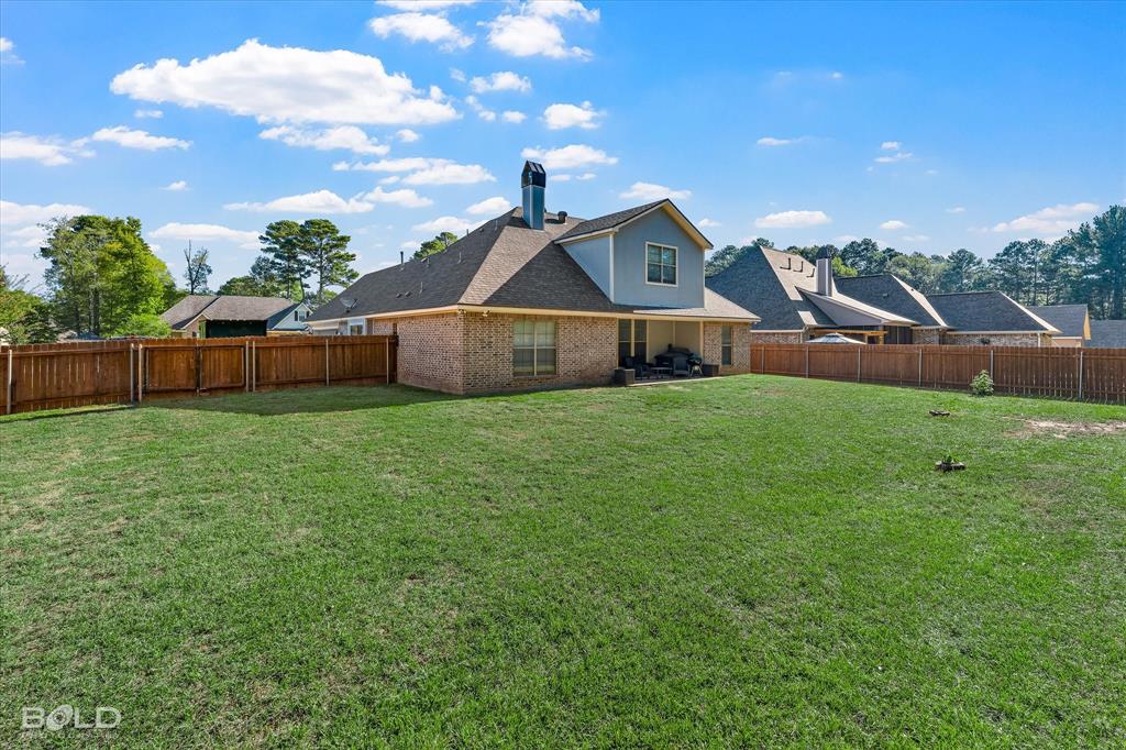 Expansive backyard featuring a manicured lawn, full-perimeter wood fencing, brick and lap siding exterior, and a chimney stack
