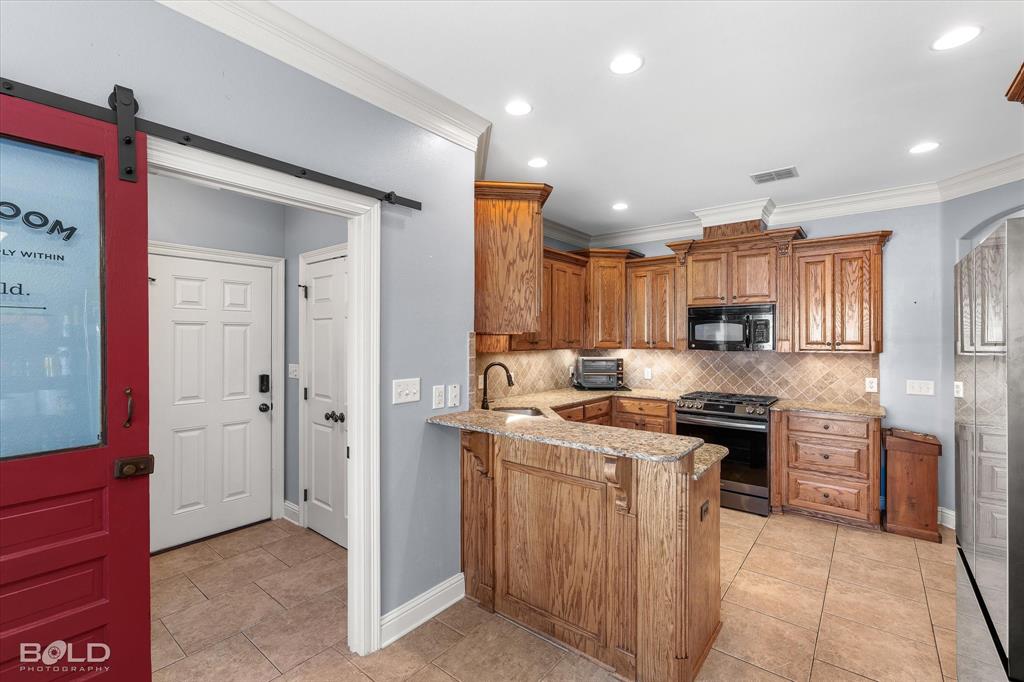 Kitchen featuring stained wood cabinetry, stone-finish countertops, tile backsplash, recessed lighting, and a red-finished sliding barn door