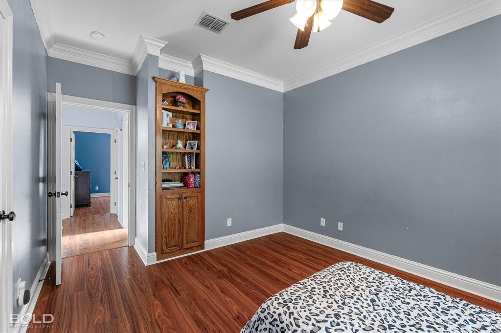 Room featuring wood-finish flooring, built-in wooden cabinetry, crown molding, and a ceiling fan
