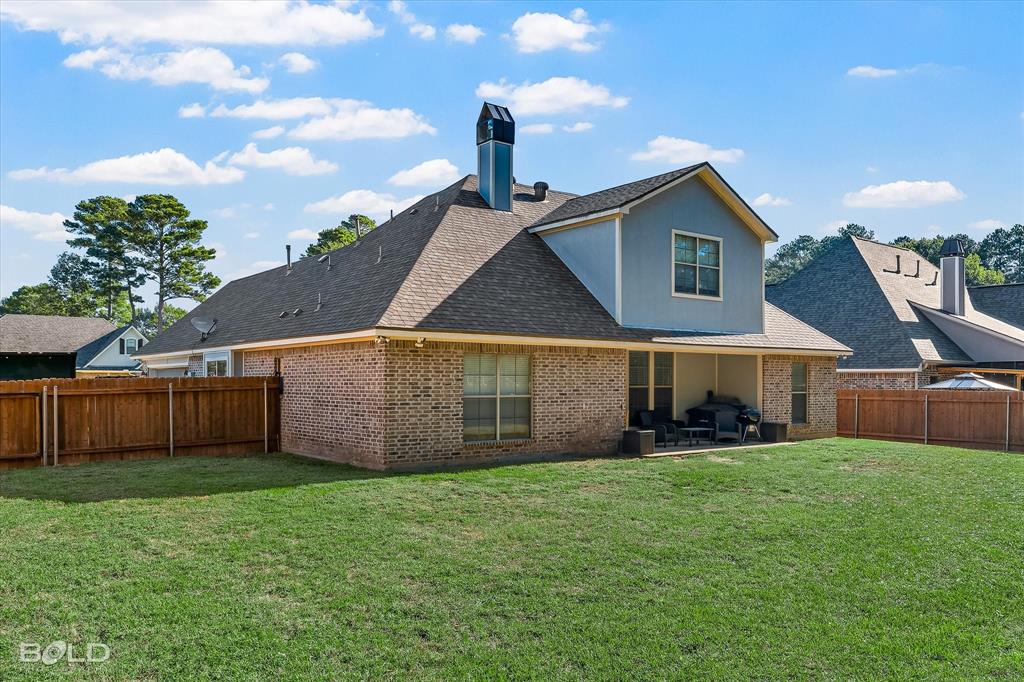 Rear exterior featuring a brick facade, covered patio, wood fencing, and a chimney