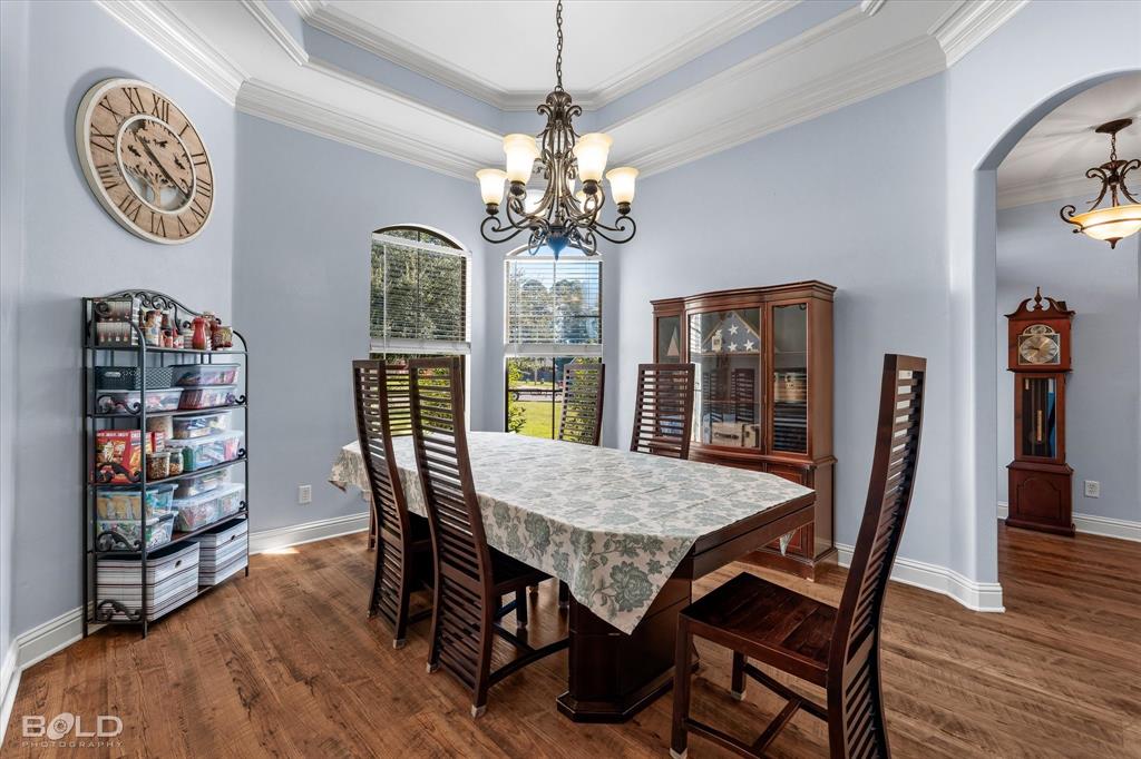 Dining area featuring a recessed tray ceiling, wood-finish flooring, multi-light decorative chandelier, and arched wall openings