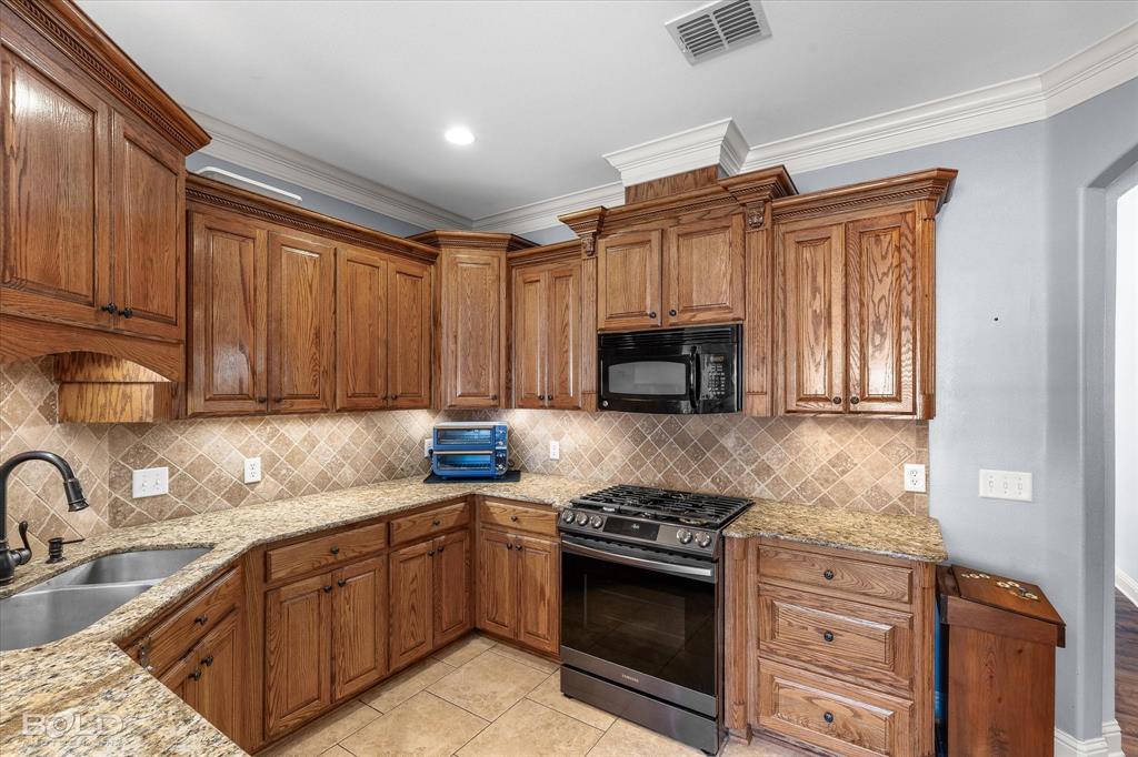 Kitchen featuring stained wood cabinetry, stone-surface countertops, diamond-pattern tile backsplash, crown molding, and stainless steel appliances
