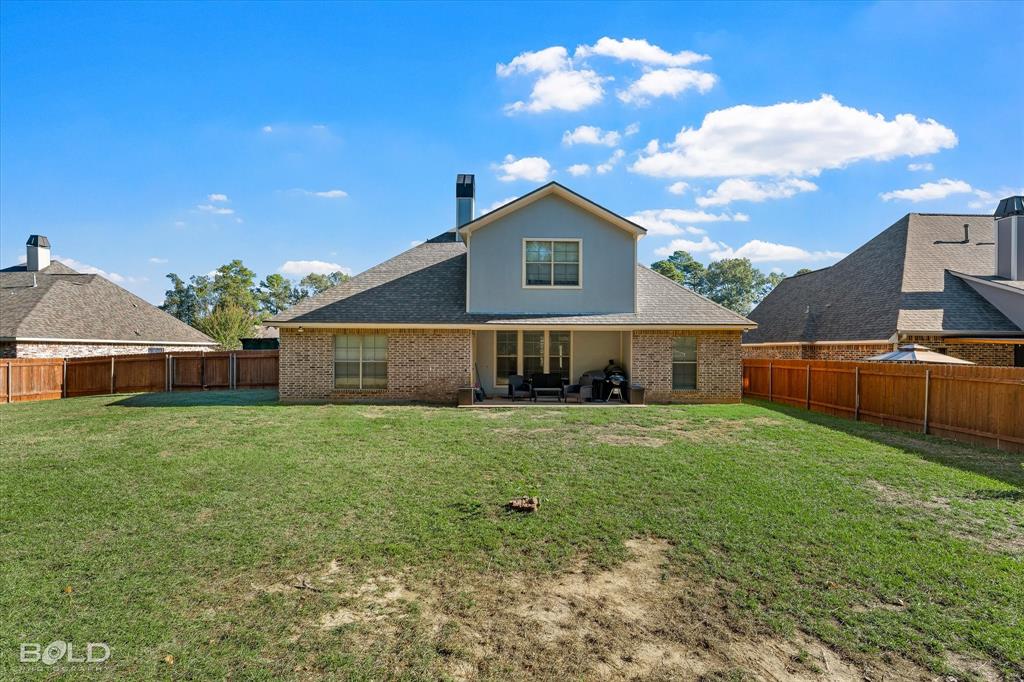 Expansive backyard featuring a grass lawn, full perimeter wood fencing, a brick exterior, and a covered patio