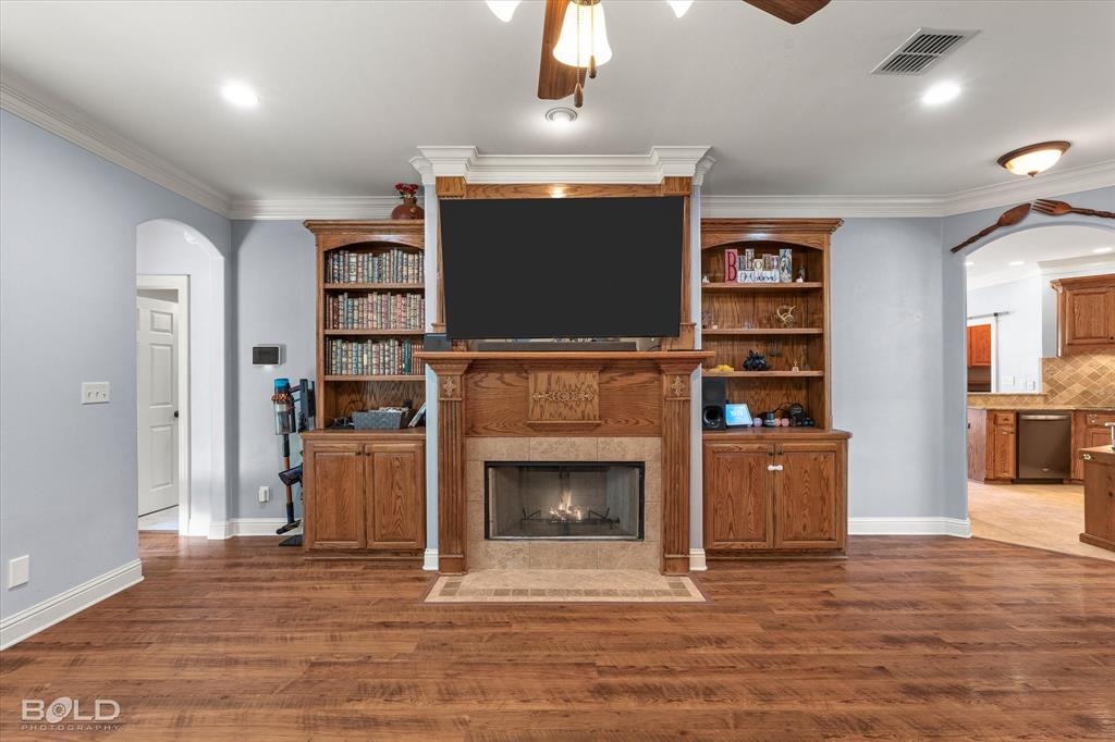 Living area featuring wood-finish flooring, custom built-in wood cabinetry with integrated shelving, and a central fireplace with stone-tile surround