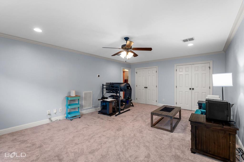 Spacious room featuring wall-to-wall carpeting, crown molding, a central ceiling fan with integrated lighting, and two sets of double-panel closet doors