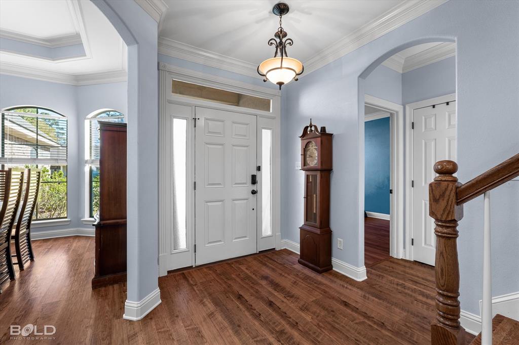 Entryway featuring wood-finish flooring, vaulted ceiling, arched architectural detailing, crown molding, and a paneled front door with sidelights and transom window