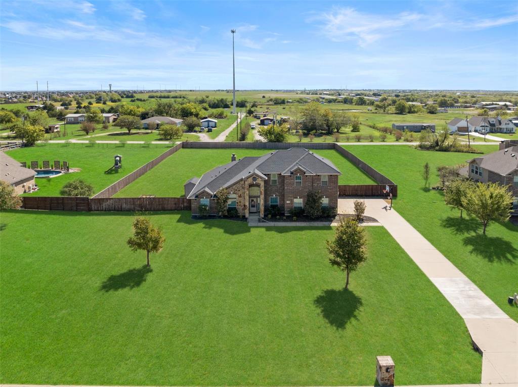 Multi-level brick exterior featuring a multi-gabled roofline, an expansive lawn, a concrete driveway, and a fenced backyard