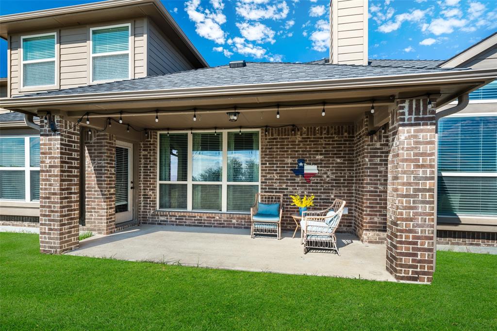 Covered concrete patio featuring brick exterior columns, multi-pane windows, and a shingle roof