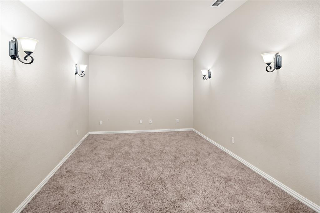Neutral-toned interior space featuring vaulted ceilings, wall-to-wall carpeting, and four decorative wall-mounted light fixtures