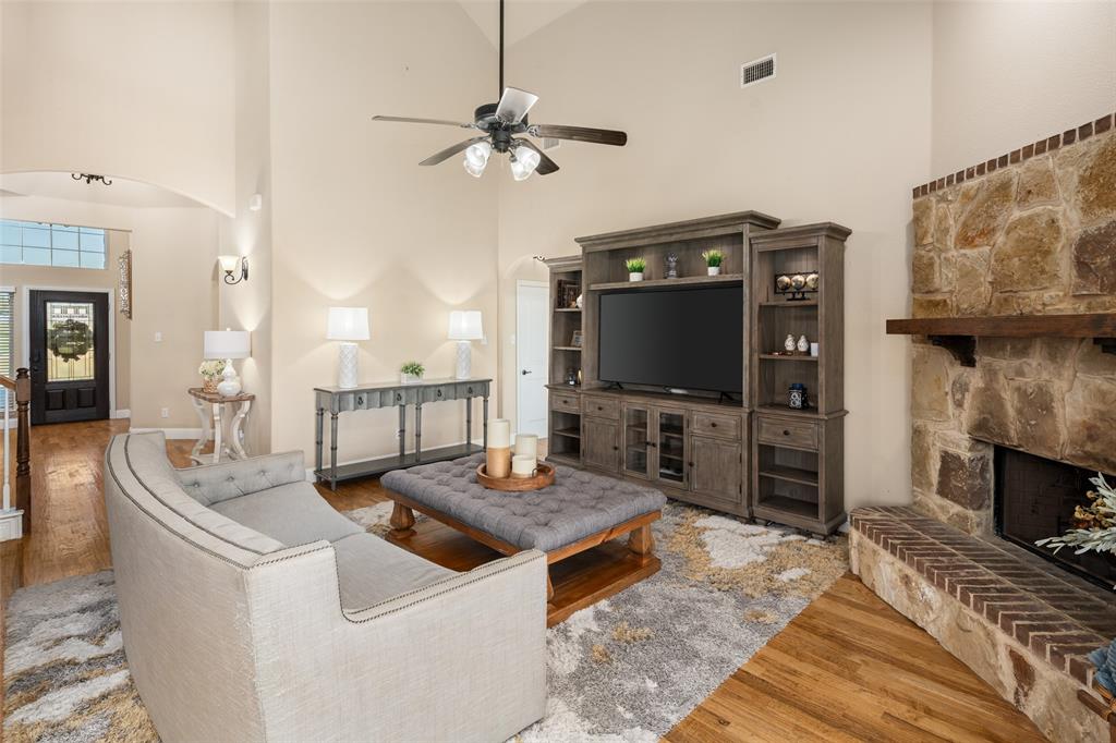 Vaulted ceiling featuring a ceiling fan, floor-to-ceiling stone fireplace with a wood mantel, brick hearth, and wood-finish flooring Vaulted ceiling featuring a ceiling fan, floor-to-ceiling stone fireplace with a wood mantel, brick hearth, and wood-finish flooring