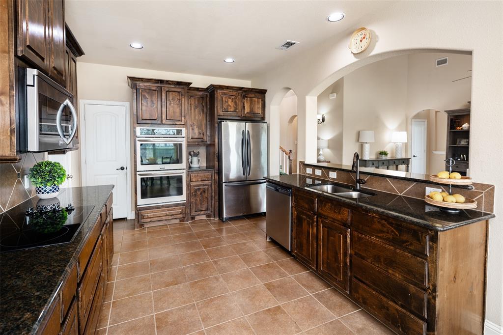Kitchen featuring dark-stained cabinetry, integrated stainless steel appliances, dual wall ovens, dark stone countertops, and tile flooring
