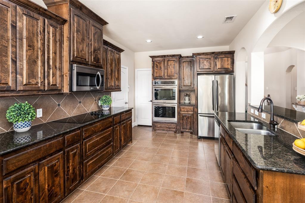 Kitchen featuring dark wood cabinetry, stone countertops, tiled backsplash, stainless steel double wall ovens, and stainless steel refrigerator