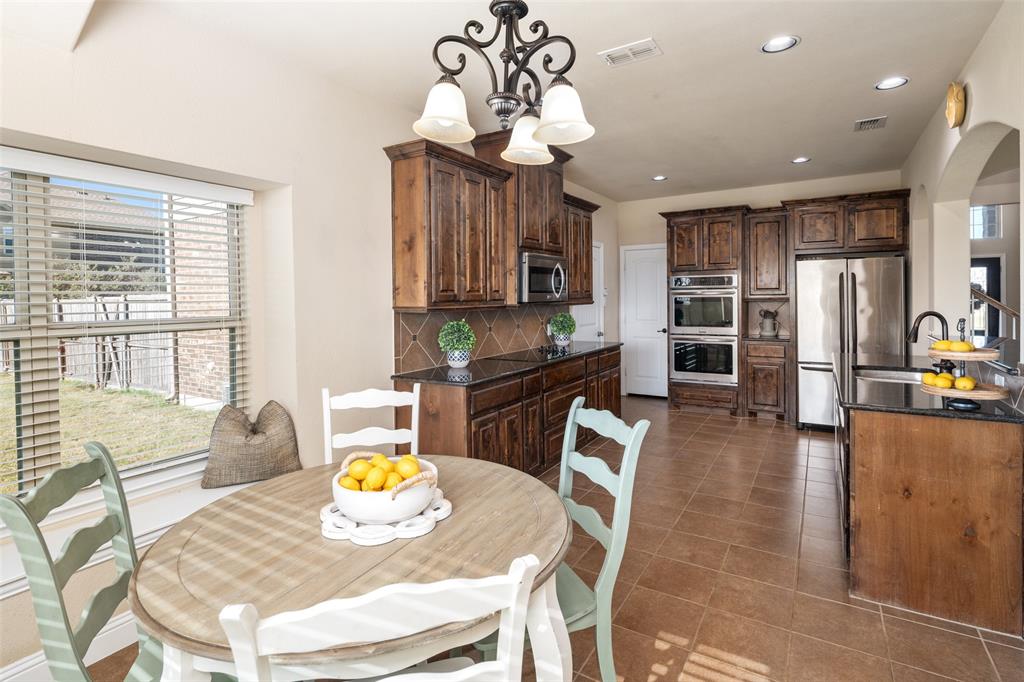 Kitchen featuring dark-stained wood cabinetry, stone countertops, tiled backsplash, integrated stainless steel appliances including a built-in double oven, and tile flooring