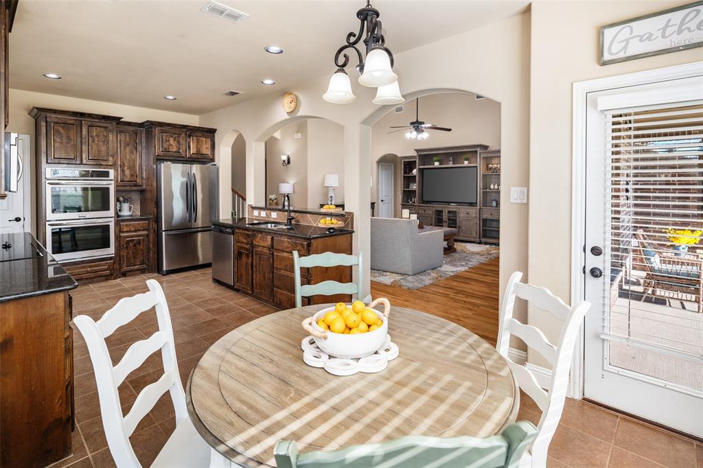 Kitchen featuring dark wood cabinetry, stainless steel appliances, built-in double oven, dark stone countertops, and tile flooring with recessed lighting