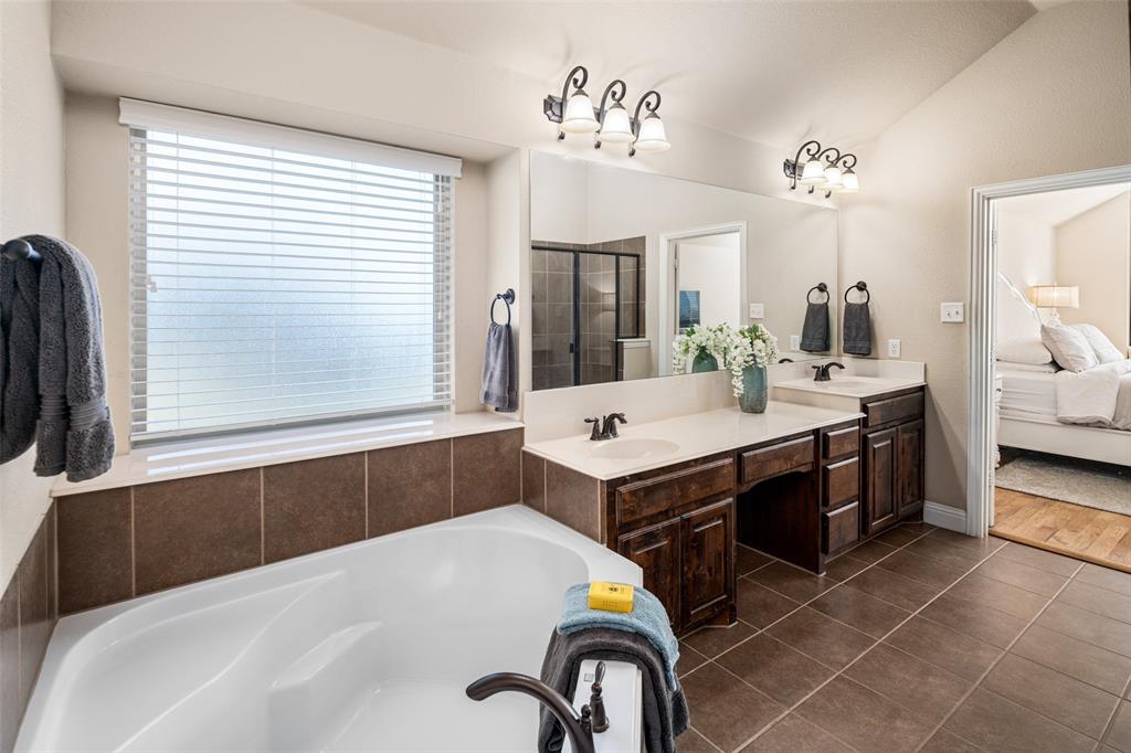 Bathroom featuring a soaking tub with tile surround, dual-sink vanity with dark-stained cabinetry, large vanity mirrors, and ceramic tile flooring