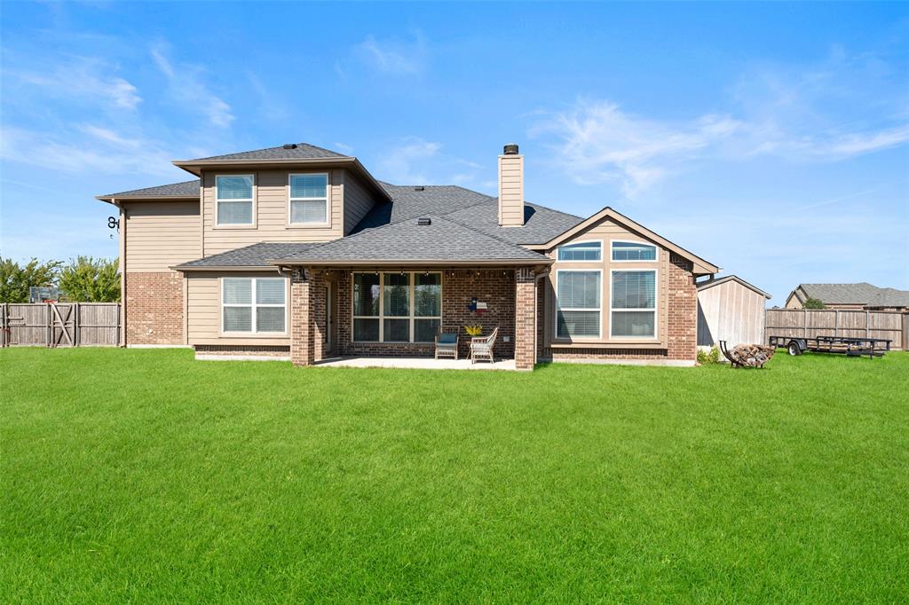 Two-story residence featuring a brick and siding exterior, a covered rear patio, a chimney, and an expansive lawn enclosed by wood fencing