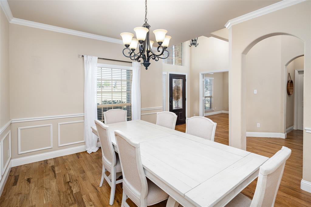 Dining area featuring wood-finish flooring, wainscoting, an arched doorway, and a multi-light chandelier