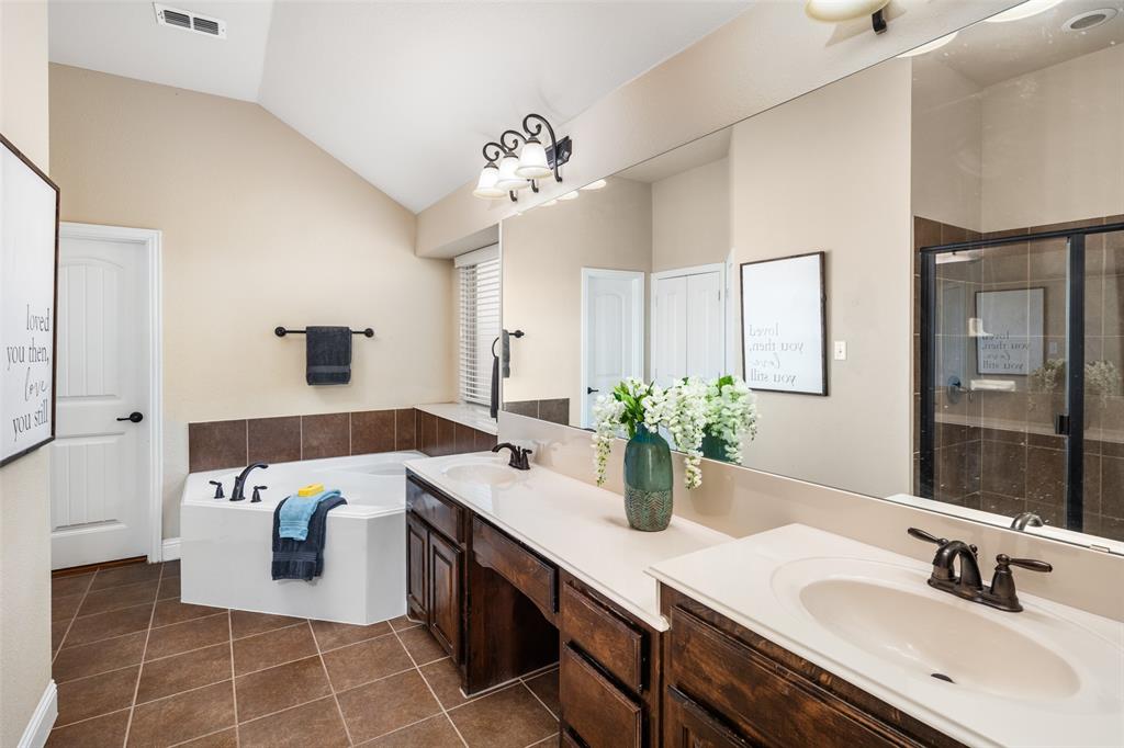 Bathroom featuring vaulted ceilings, dual-sink vanity with dark wood cabinetry, soaking tub with tile surround, walk-in shower with glass enclosure, and tile flooring