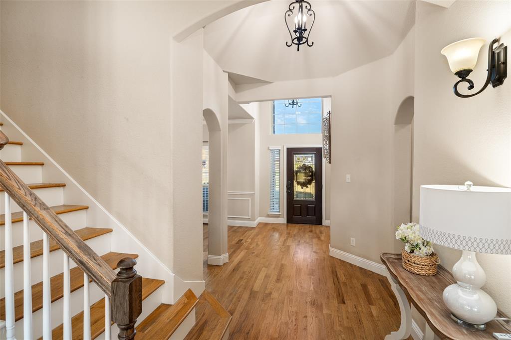 Foyer featuring high ceilings, wood-finish flooring, staircase with wood handrails, arched architectural details, and a multi-pane glass entry door Foyer featuring high ceilings, wood-finish flooring, staircase with wood handrails, arched architectural details, and a multi-pane glass entry door