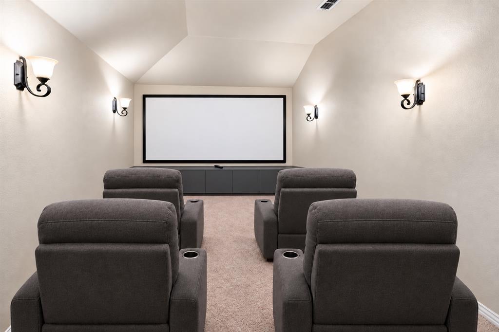 AI STAGED - Dedicated media room featuring a mounted projection screen, built-in lower cabinetry, wall-mounted sconce lighting, and a vaulted ceiling