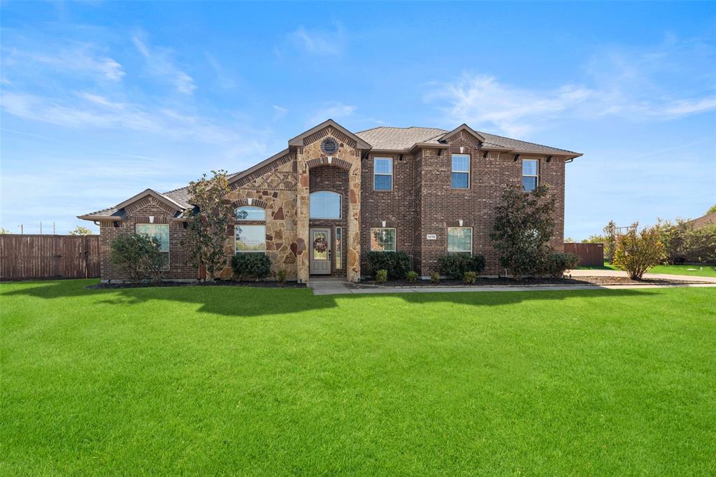 Two-story brick exterior featuring stone veneer accents, multi-gabled roofline, arched entryway, and manicured lawn