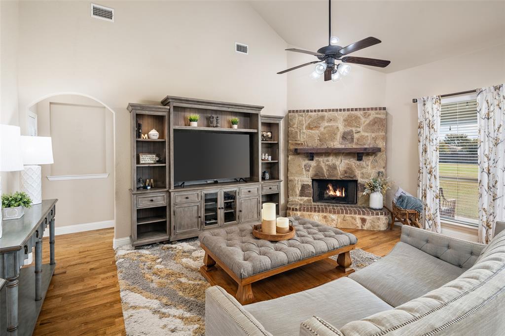 Living area featuring a vaulted ceiling, stone-surround corner fireplace with a wooden mantel, wood-finish flooring, and built-in cabinetry Living area featuring a vaulted ceiling, stone-surround corner fireplace with a wooden mantel, wood-finish flooring, and built-in cabinetry