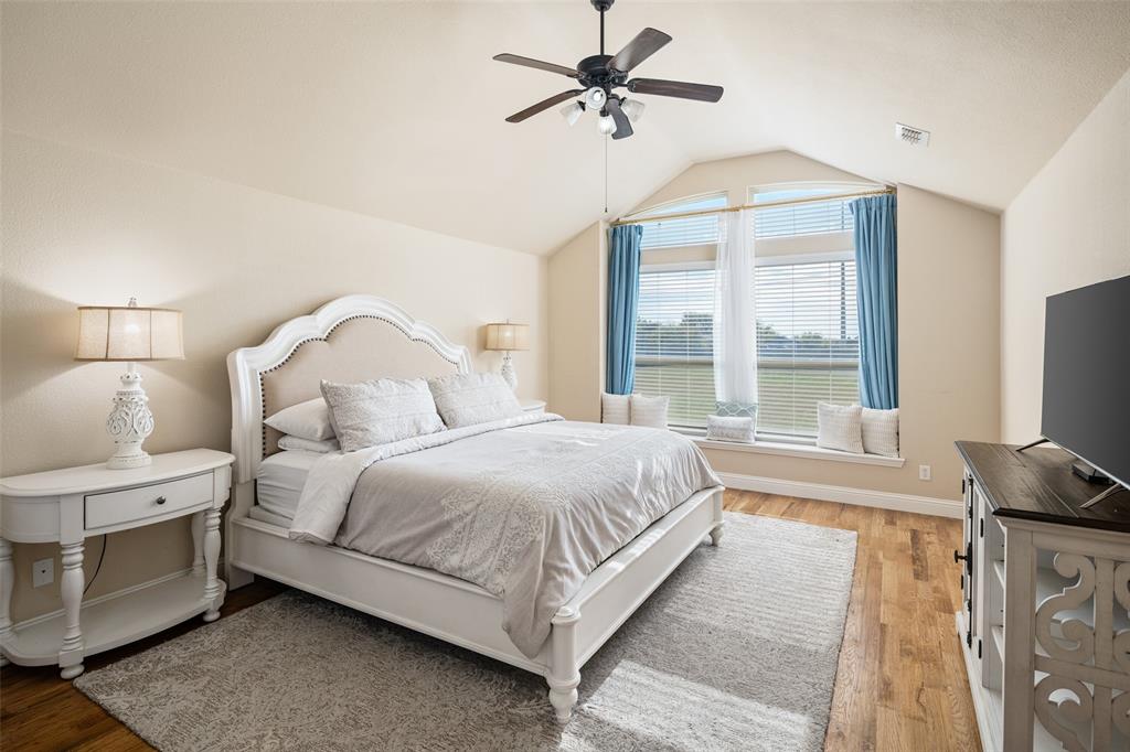 Vaulted ceiling featuring a central blade-style fan, expansive windows with a deep built-in ledge, and wood-finish flooring