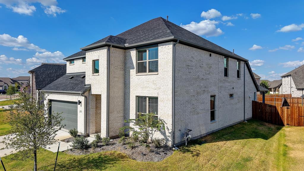Two-story brick exterior, dark composition shingle roof, attached garage with modern door, multiple windows, and a wood privacy fence