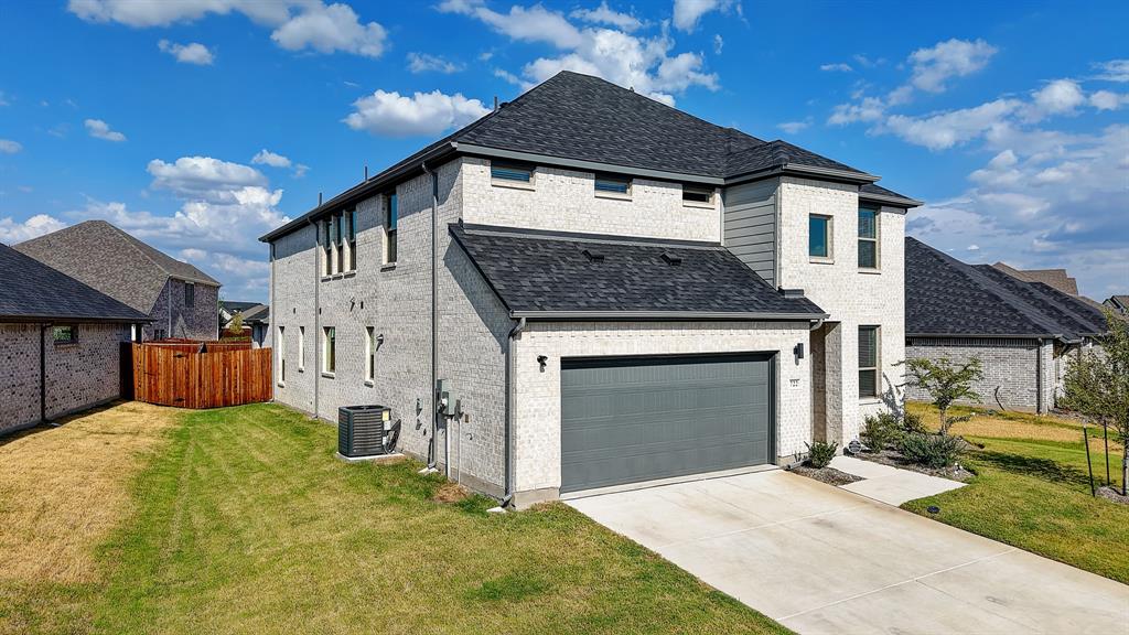 Two-story residence featuring light-colored brick exterior, dark shingles, an attached garage with a dark door, and a concrete driveway
