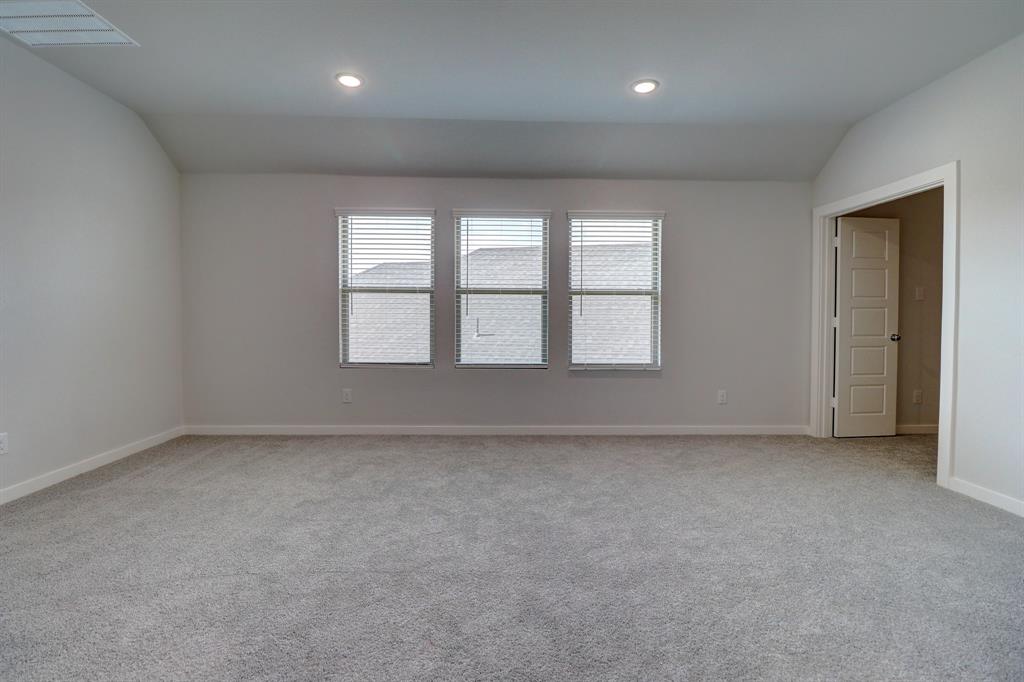 Spacious room featuring gray carpeting, multiple windows with blinds, recessed ceiling lighting, and an architectural vaulted ceiling detail