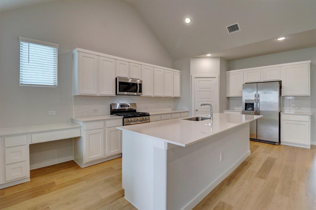 Kitchen featuring wood-finish flooring, vaulted ceiling, white cabinetry, stainless steel appliances, and a central island with an undermount sink