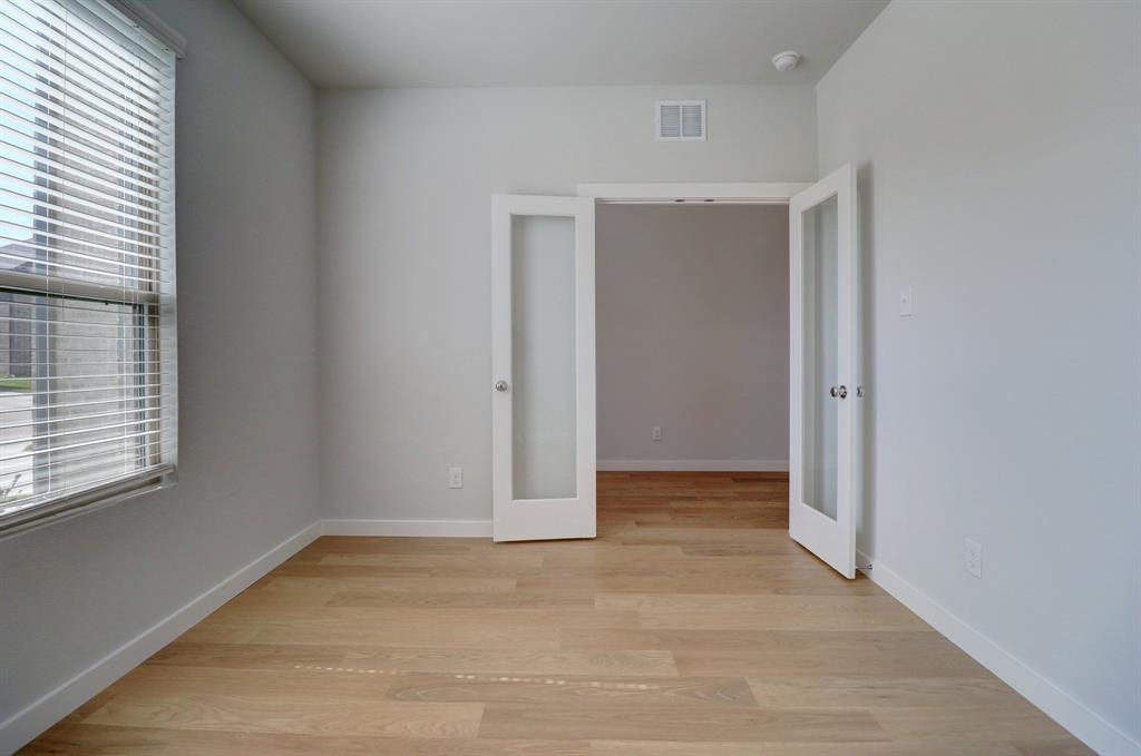 Light wood-finish flooring, white walls, double French doors with frosted glass, and a large window with blinds
