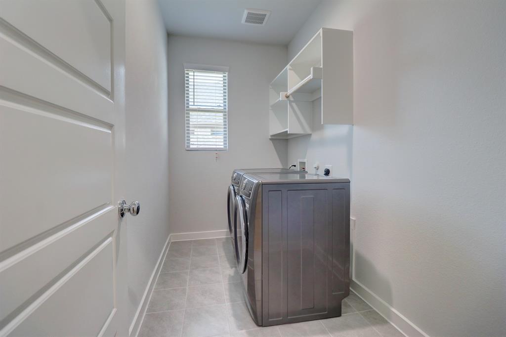 Laundry area featuring wall-mounted shelving, tiled flooring, and a window with horizontal blinds