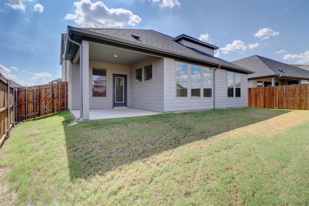 Expansive backyard featuring a covered patio with concrete flooring, a full wood privacy fence, and a large grass lawn