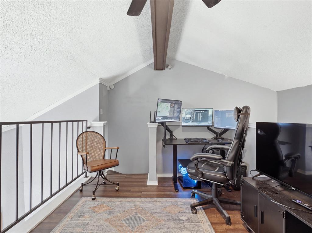 Vaulted ceilings with exposed structural beam, dark wood-finish flooring, and black metal railing