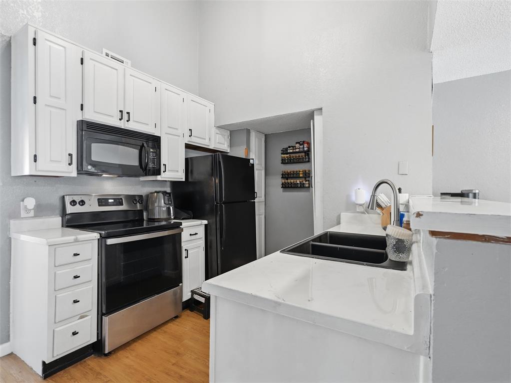 Kitchen featuring white cabinetry, solid-surface countertops, dual-basin sink with high-arc faucet, and stainless steel appliances