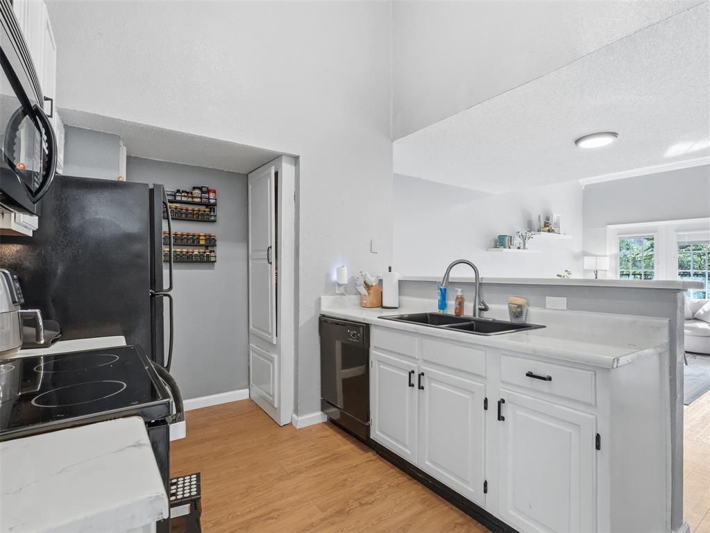Kitchen featuring white cabinetry, stone-finish countertops, a dual-basin sink with a gooseneck faucet, black appliances, and wood-finish flooring
