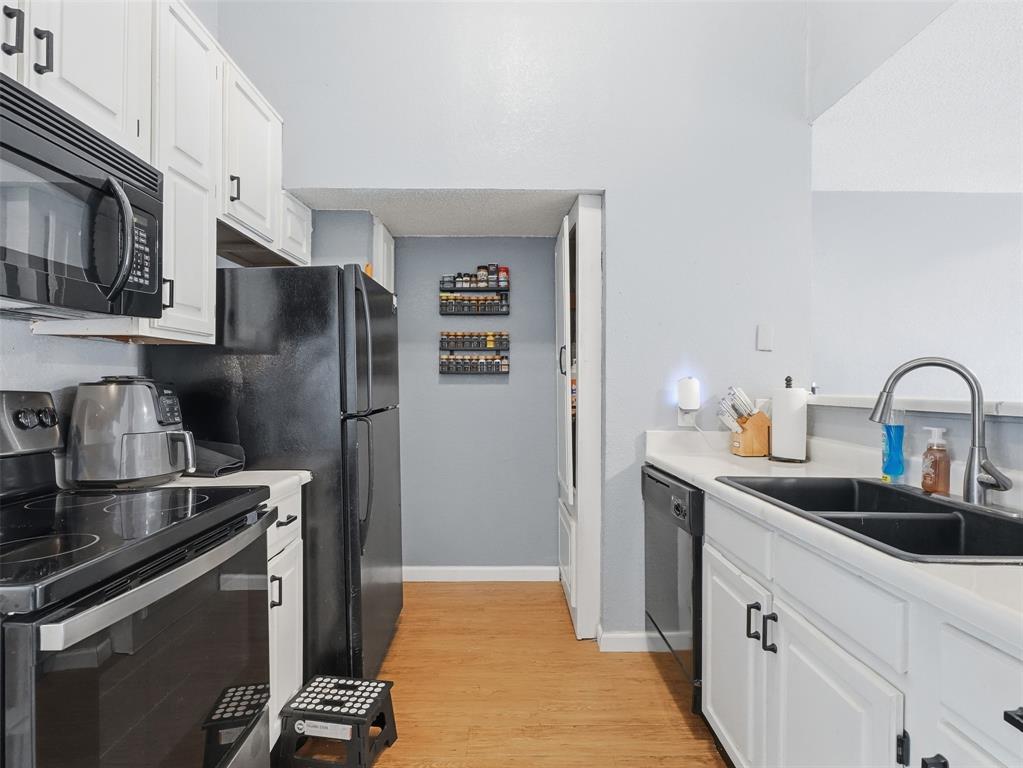 Kitchen featuring white shaker-style cabinetry, wood-finish flooring, black appliances, a dual-basin sink with a gooseneck faucet, and solid-surface countertops