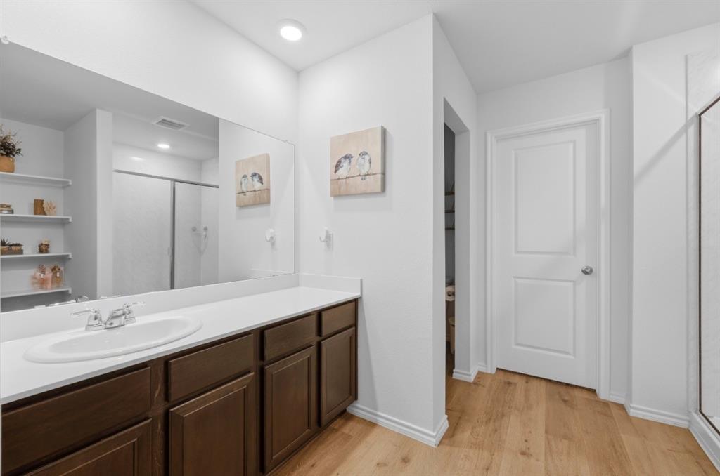 Bathroom featuring a dark wood-finish vanity, solid surface countertop with an integrated oval sink, full-width wall mirror, wood-finish flooring, and built-in shelving