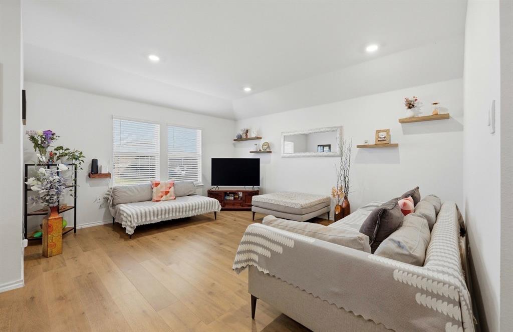 Living area featuring vaulted ceilings, wood-finish flooring, recessed lighting, and wall-mounted wood floating shelving