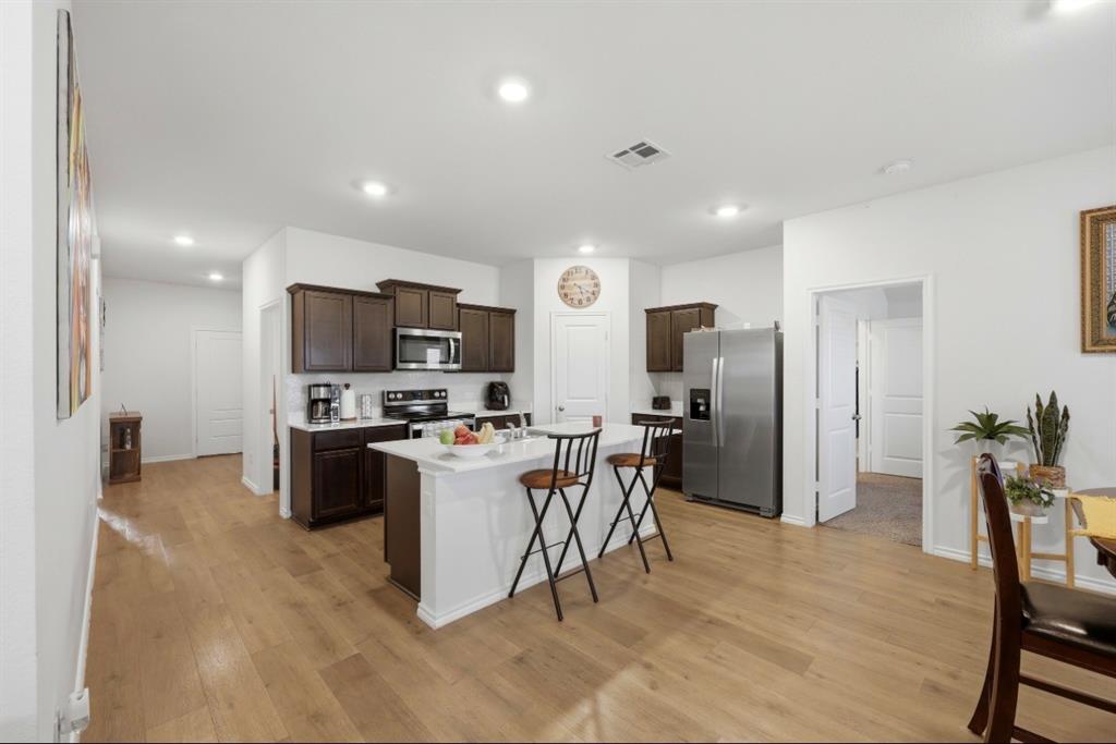 Kitchen featuring dark-toned cabinetry, stainless steel appliances, a central island with white stone-finish countertop, and wood-finish flooring