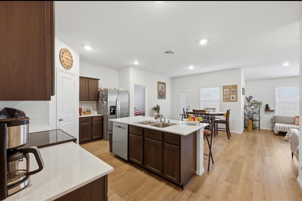 Kitchen featuring wood-finish cabinetry, white countertops, a center island with a dual-basin sink, stainless steel appliances, and wood-finish flooring